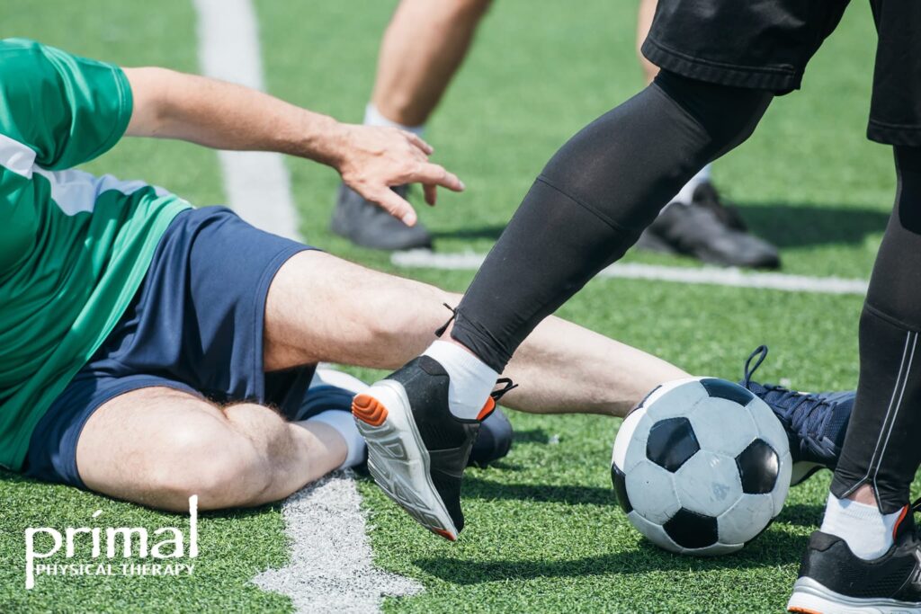 Close-up of two soccer players colliding during a game, with one player sliding on the turf and the other blocking the ball, highlighting a potential sports injury scenario.